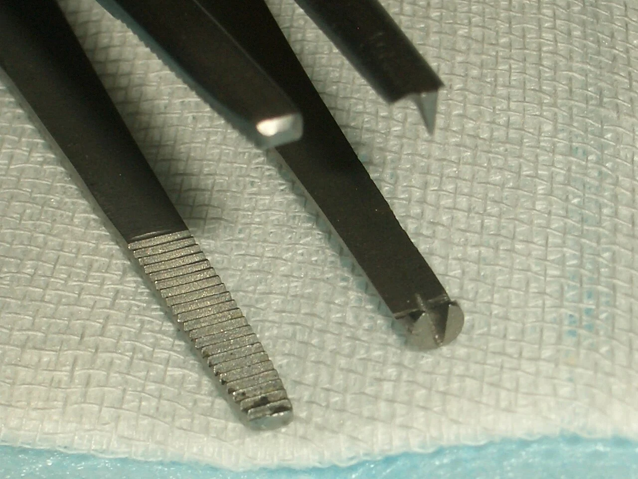 Thumb-forceps tip comparison: prominent interlocking teeth are visible on the right.